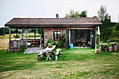 Weathers table and bench set on lawn in front of rustic, wooden weekend house