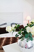 weiße Rosen in bauchiger, verzierter Bauernsilbervase; im Hintergrund Doppelbett