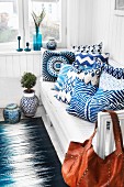 White and blue patterned scatter cushions on bench in corner against white, wood-clad walls