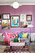 Ottoman, couch with curved backrest and colourful scatter cushions below collection of pictures on wall with purple wallpaper