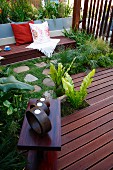 Objets d'art on side table on wooden deck; bench with cushions in background