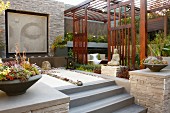 Meditation garden with bowls of succulents on walls flanking steps, Buddha artwork on stone wall and separate planted area