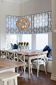 Dining set in window bay with window seat, patterned roller blinds and white-painted chairs