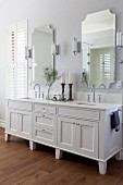 White washstand with twin sinks below two mirrors flanked by sconce lamps
