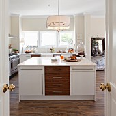Blick durch offene Flügeltür auf freistehenden Mittelblock mit Unterschränken in Weiß und aus Holz, in offener Küche