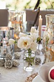 White roses in glass bottle amongst silver candle lanterns and Christmas decorations