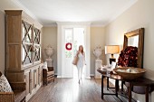 Elegant foyer with glass-fronted dresser, Christmas wreath on table and woman walking in through open front door
