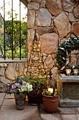 Christmas atmosphere in garden, lit candle in flower pot and obelisk covered in fairy lights in front of stone wall