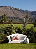 White, outdoor sofa with ethnic scatter cushions in garden in front of mountain landscape