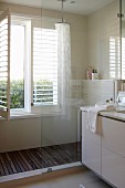 Ausschnitt eines modernen Bades, teilweise sichtbarer Waschtisch neben verglastem Duschbereich, vor Fenster