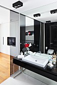 Ensuite bathroom - black washstand with white sink against mirrored wall and tinted glass panel to one side with view into bedroom