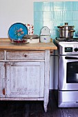 Rustic cabinet next to free-standing, stainless steel cooker with pale blue tiled splashback