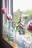 Delicate pink tulips and peonies in various glass vessels on narrow windowsill