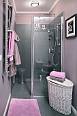 An open shower in an elegant bathroom with grey tiles, lilac-grey walls and lilac coloured towels