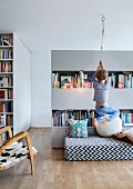 Open-plan interior with child climbing rope suspended from ceiling, black and white patterned futon and partition shelving