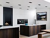 Elegant, monolithic counter with wooden front in front of white fitted cupboards with fitted appliances