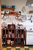 Vintage kitchen with collection of colanders on shelves and hooks and open-fronted, cluttered wooden base cabinet
