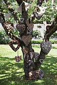 Various heart-shaped wreaths hanging on tree decorated with bunting in garden