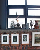 Collection of pewter jugs on sill of blue window above artistic hand prints on clipboards on brick wall