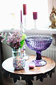 Stillleben mit lilafarbener Glasschale und Windlicht auf antikem Tisch mit Schnitzerei