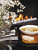 Schale mit Suppe und Brotscheibe auf Holzbrett