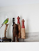 Vintage figurines of humans, miniature wooden sculptures and stuffed parrot under glass cover