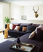 Black corner sofa with many scatter cushions in front of hunting trophy on wall