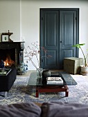 Low coffee table with smoked glass top on vintage-look rug in front of double doors painted dark grey