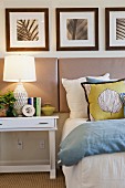 Lit table lamp with picture frames by cropped bed; San Marcos; California; USA