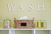 Schriftzug Wash in Waschküche über Regal mit Korb, Glasbehälter mit Wäscheklammern & Waschmittelflaschen