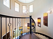 Flurbereich mit kreisförmiger Decke & Wendeltreppe dekoriert mit Wandleuchten und abstrakten Wandbildern