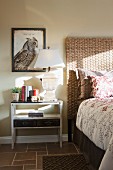 Schlafzimmer mit Nachttisch, Tischleuchte & Wandbild mit Vogelmotiv neben Bett mit geflochtenem Kopfteil