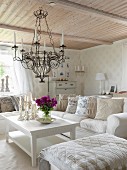Ottoman and sofa around white coffee table below wrought iron candle chandelier hanging from wooden ceiling in rustic living room