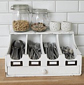 Storage jars and tealight holders on old, white-painted cutlery tray with drawer