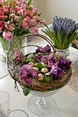 Arrangement of moss, violas and quail eggs in glass goblet, bouquet of tulips and grape hyacinths on dining table
