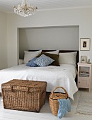 Wicker trunk at foot of double bed with headboard in niche in white bedroom