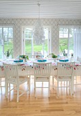 Floral chandelier above table festively set with floral tablecloth in white dining room