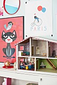 Colourful children's posters on wall and doll's house on cabinet
