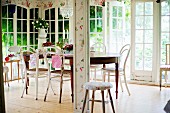 Thonet chairs with white, peeling paint around antique wooden table in conservatory
