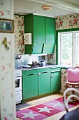 Kitchen cabinets with green doors and rug with star motif on wooden floor
