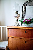 Paraffin lamp and bowl of flowers on simple wooden chest of drawers