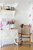 Wooden rocking chair next to vase of flowers on white, ornate cabinet
