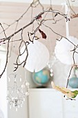 Glass ornaments and white baubles hanging from ornamental branch