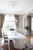White armchairs and chairs with carved backrests around table in open-plan dining area of villa