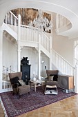 White staircase and balustrade in foyer of country-house villa; 50s armchair and side table on Oriental rug
