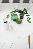 Sprigs of leaves in various vases and decorative, green glass spheres on white coffee table