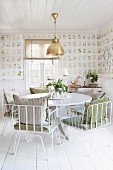 White metal chairs with cushions at round table in dining room with botanical wallpaper and white wooden floor