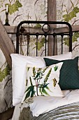 Green and white scatter cushion on black metal bed against half-timbered wall with wallpapered panels with botanical pattern