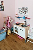 Toy kitchen and blue-painted bracket shelf on pink-painted wall in corner of child's bedroom