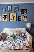 Patchwork blanket and scatter cushions on armchair bed below pictures on blue-painted wall